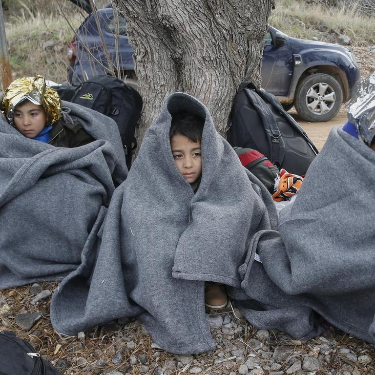 Neu angekommene Flüchtlinge aus Syrien auf der griechischen Insel Lesbos. Kinder sitzen dich eingehüllt am Fuß eines Baumes.