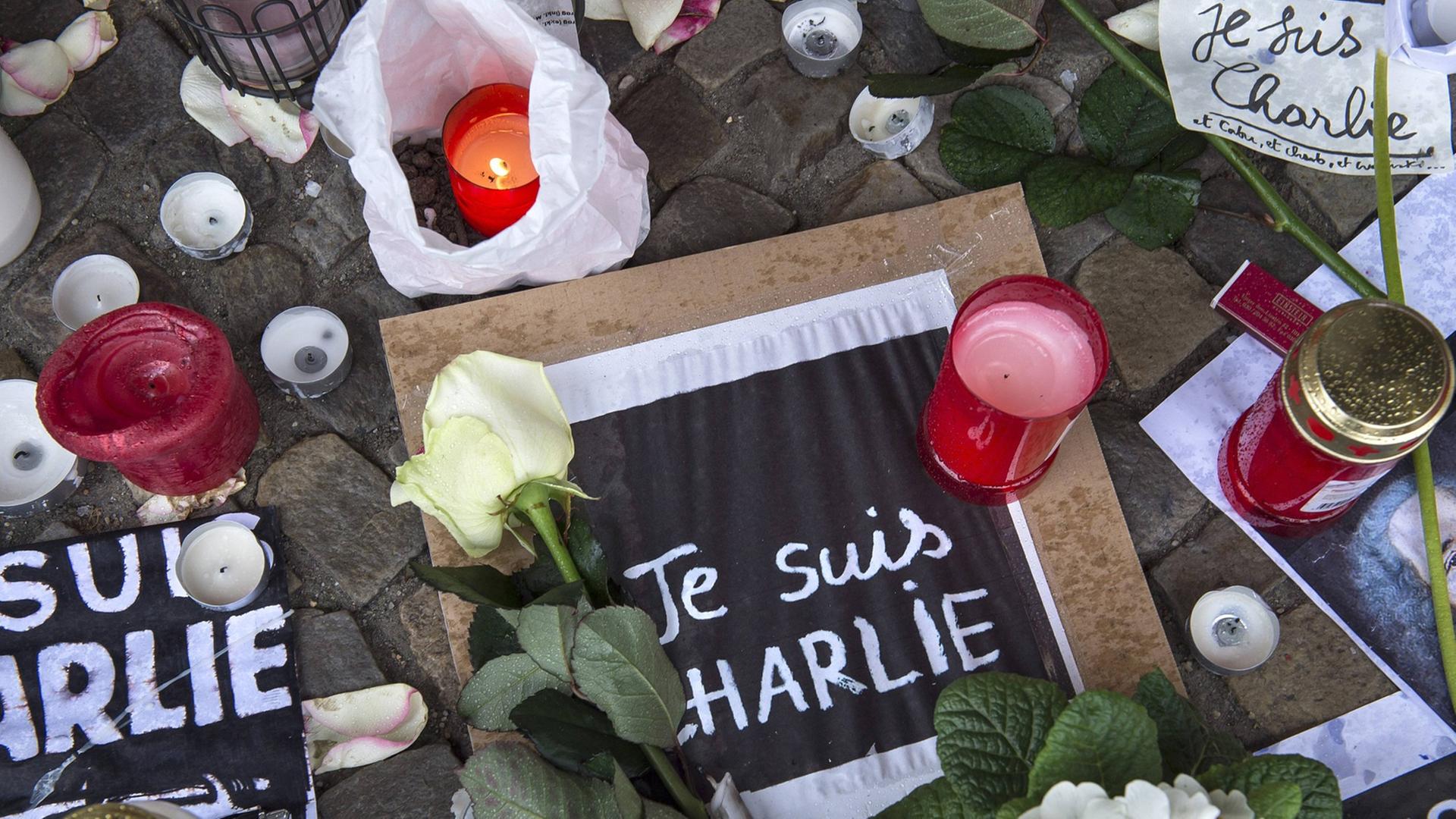 Blumen und Kerzen und Zettel mit der Aufschrift "Je suis Charlie" liegen auf dem Boden. Blumen und Kerzen und Zettel mit der Aufschrift "Je suis Charlie" liegen auf dem Boden.