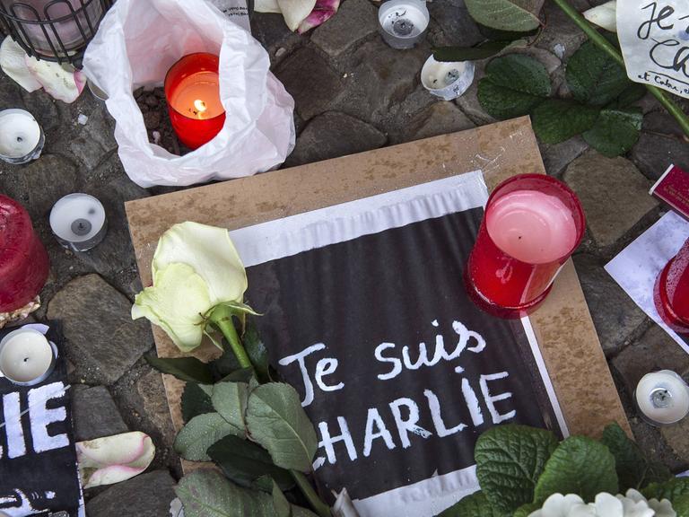 Blumen und Kerzen und Zettel mit der Aufschrift "Je suis Charlie" liegen auf dem Boden.