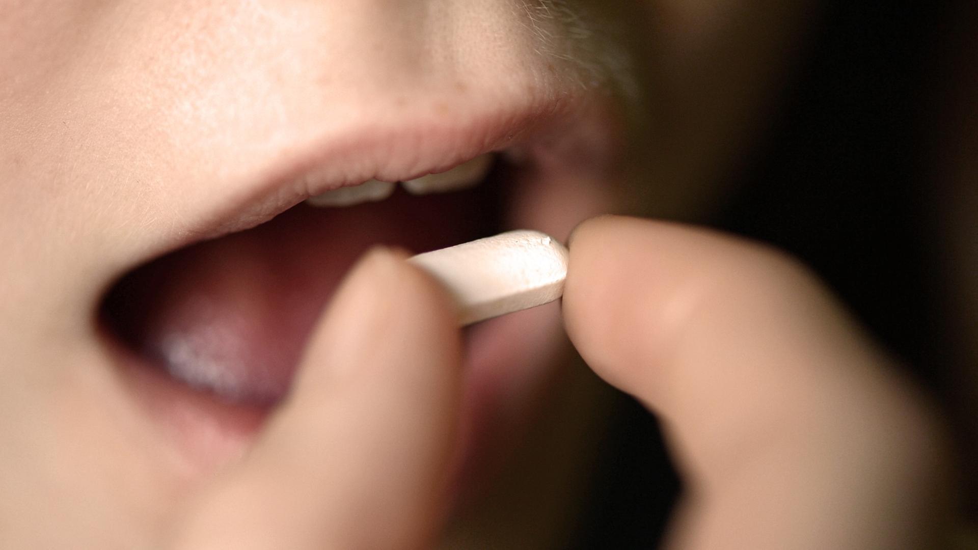 Ein Mädchen nimmt eine weiße Tablette in den Mund.