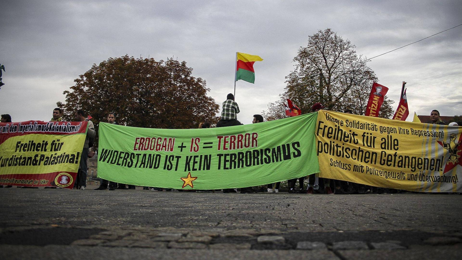 Demonstranten halten Banner hoch. Auf dem Banner, das im Zentrum des Bildes zu sehen ist steht: "Erdogan + IS = Terrorismus. Widerstand ist kein Terrorismus". Einer der Demonstranten hält eine kurdische Flagge hoch. Demonstranten halten Banner hoch. Auf dem Banner, das im Zentrum des Bildes zu sehen ist steht: "Erdogan + IS = Terrorismus. Widerstand ist kein Terrorismus". Einer der Demonstranten hält eine kurdische Flagge hoch.