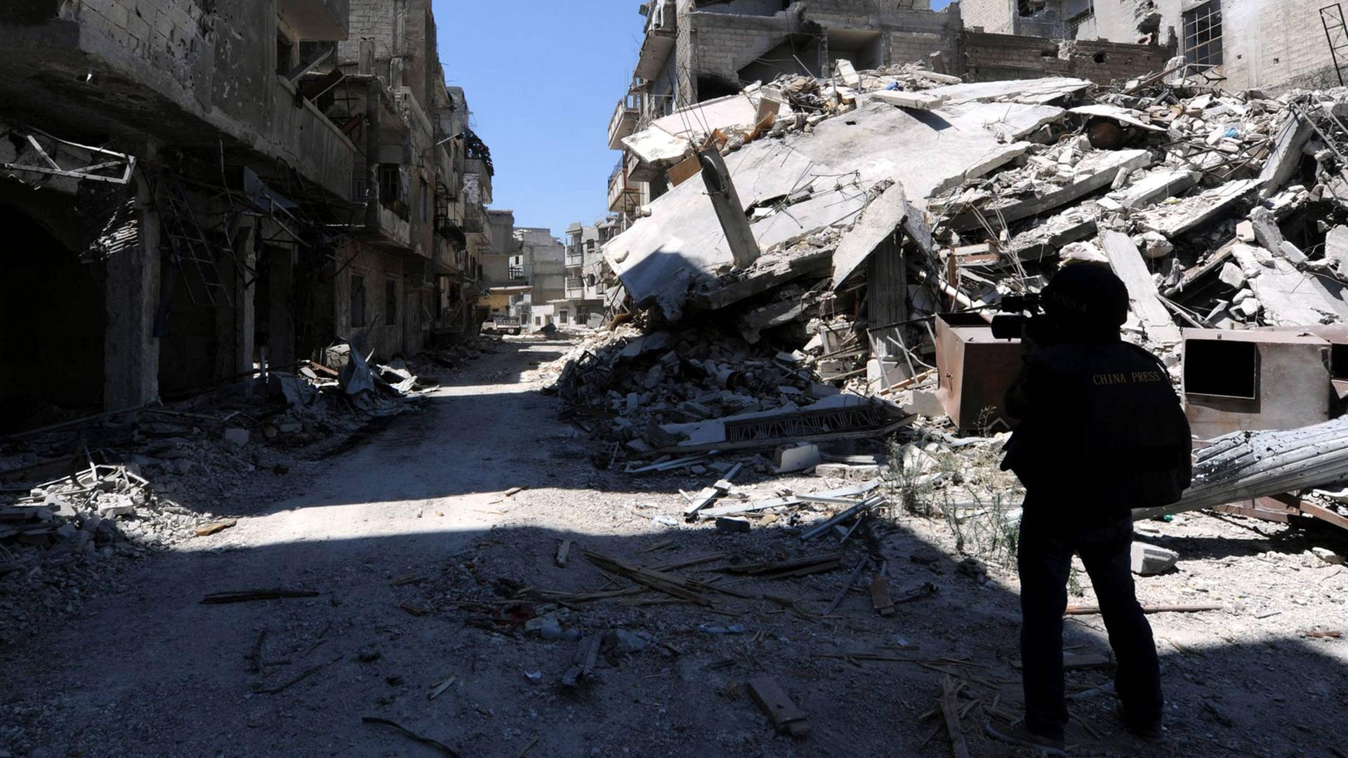 Ein Journalist läuft mit einer Kamera eine zerstörte Straße in der Homs-Provinz in Syrien lang