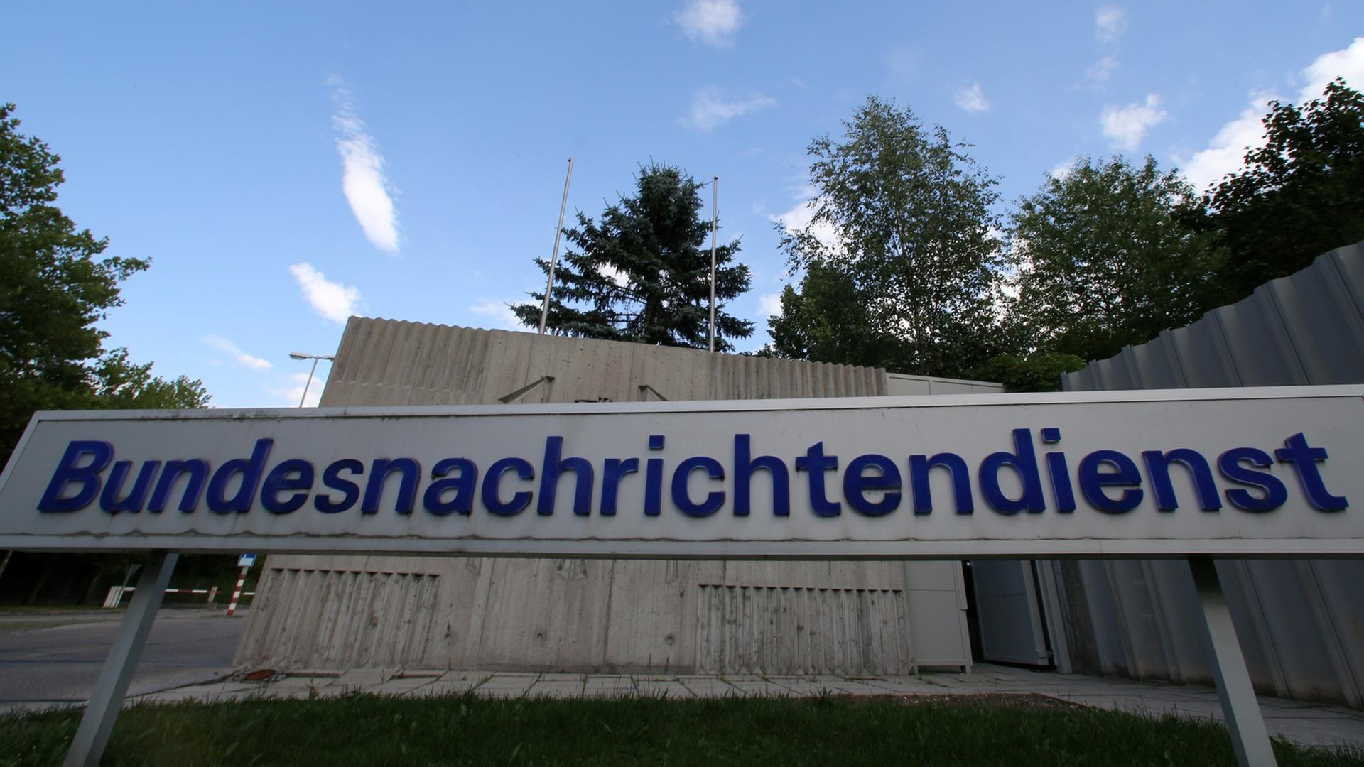 Graues Schild mit blauer Aufschrift "Bundesnachrichtendienst" vor einer grauen Mauer und blauem Himmel Graues Schild mit blauer Aufschrift "Bundesnachrichtendienst" vor einer grauen Mauer und blauem Himmel