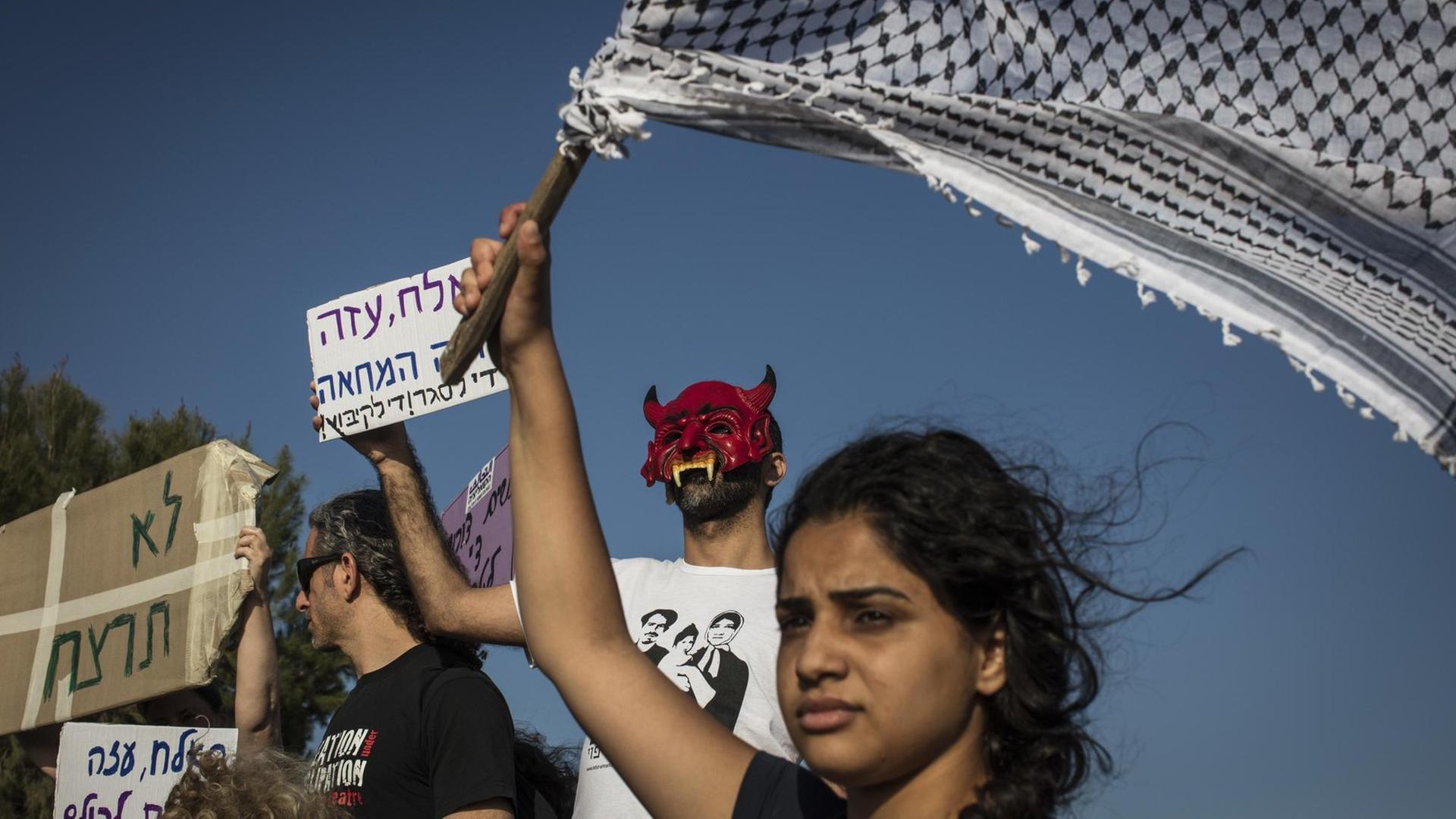 Israelische und palästinensische Aktivisten halten bei einer Solidaritätsbekundung für Gaza auf der israelischen Seite der Grenze zwischen dem Gazastreifen und Israel Schilder und eine Kufiya hoch.