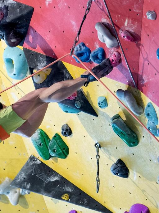 Christoph Hanke klettert im März 2018 mit einem Seil gesichert an einer Kletterwand. Sein rechtes Bein hängt in der Luft, mit den übrigen Extremitäten hält er sich fest und stützt sich ab.