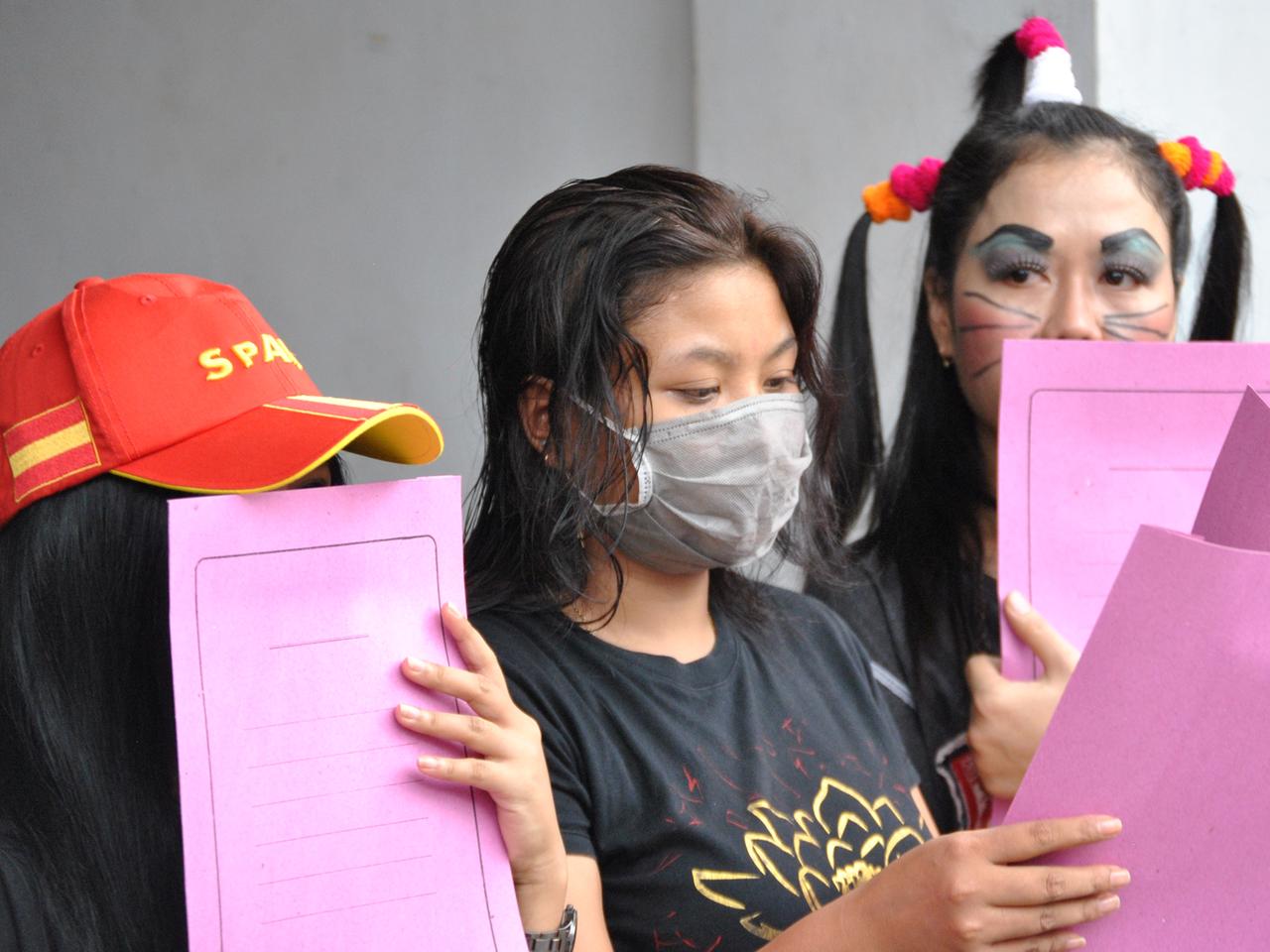 Demonstrantinnen gegen die Schließung des Rotlicht-Viertels in der Altstadt von Surabaya, der zweitgrößten Stadt Indonesiens. Sie verbergen sich hinter Mundschutz und rosa Mappen. 