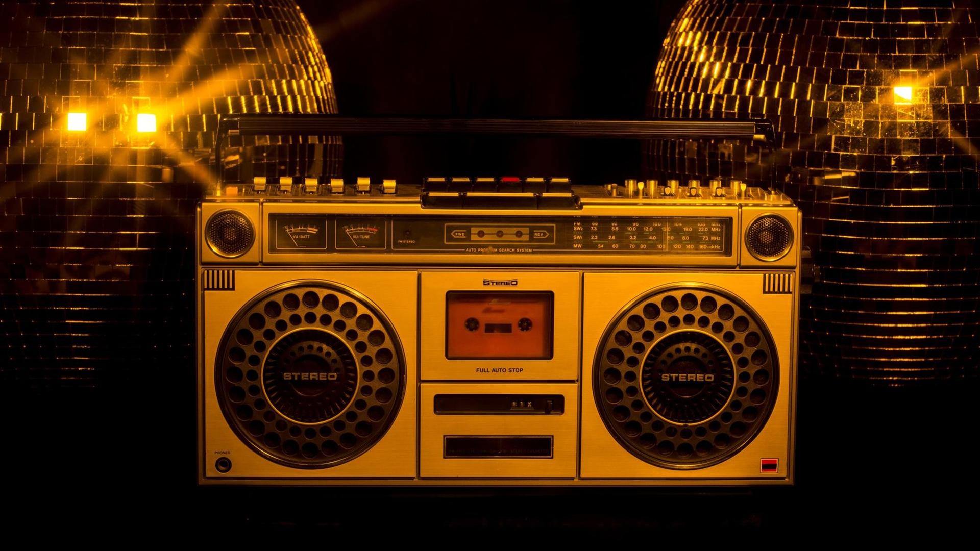 Ein Ghettoblaster steht vor zwei goldenen Discokugeln. Ein Ghettoblaster steht vor zwei goldenen Discokugeln.