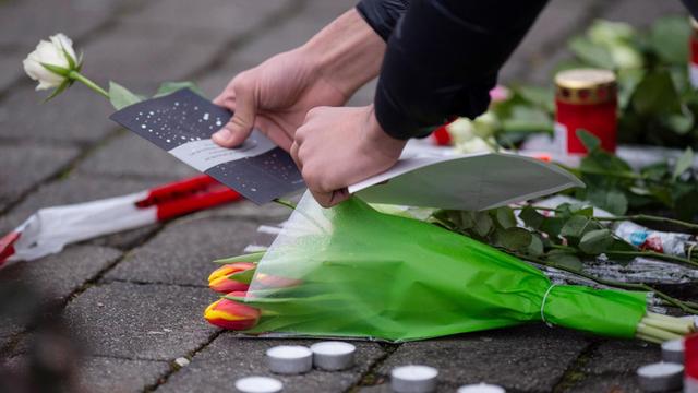 Eine Frau legt als Zeichen der Trauer eine Karte und Blumen an einem Tatort in Hanau nieder.