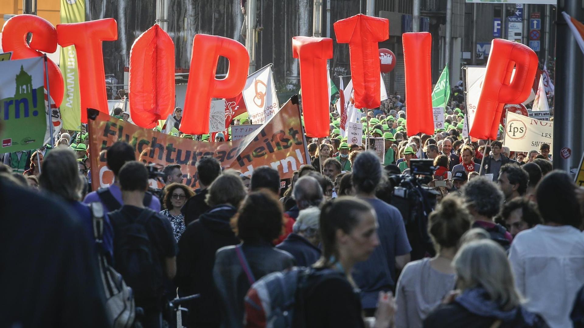 Menschen ziehen durch die Brüsseler Innenstadt. Einige von ihnen halten große Buchstaben in die Höhe, die die Forderung ergeben: Stop TTIP. Menschen ziehen durch die Brüsseler Innenstadt. Einige von ihnen halten große Buchstaben in die Höhe, die die Forderung ergeben: Stop TTIP.