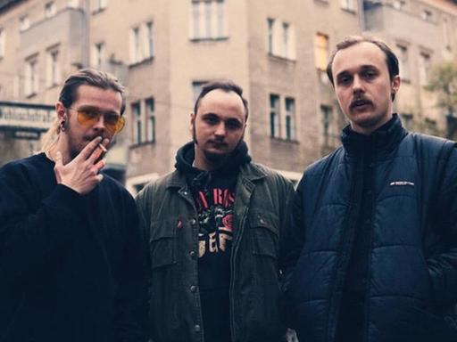 Die drei Musiker von Molchat Doma stehen nebeneinander, hinter ihnen befindet sich ein Berliner Altbau.