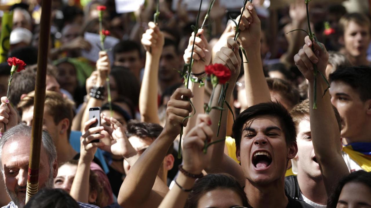 Das Bild zeigt die Köpfe mehrerer Demonstranten, von denen einige etwas rufen. Sie halten die roten Blumen in die Höhe. Das Bild zeigt die Köpfe mehrerer Demonstranten, von denen einige etwas rufen. Sie halten die roten Blumen in die Höhe.