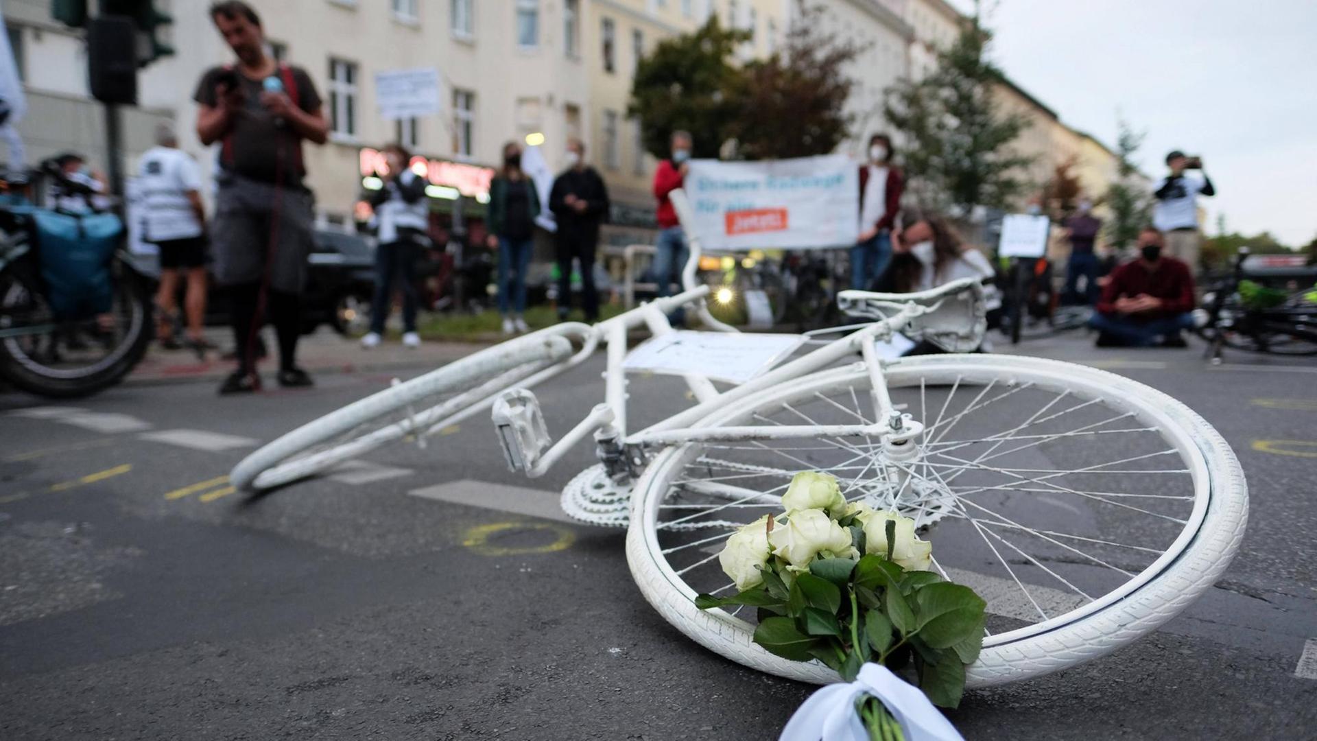 Ein weißes Fahrrad liegt auf dem Asphalt, umringt von Menschen. Ein weißes Fahrrad liegt auf dem Asphalt, umringt von Menschen.