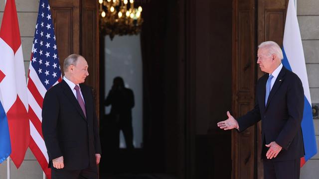 Biden und Putin stehen weit voneinander entfernt. Biden reicht seine Hand Richtung Putin.