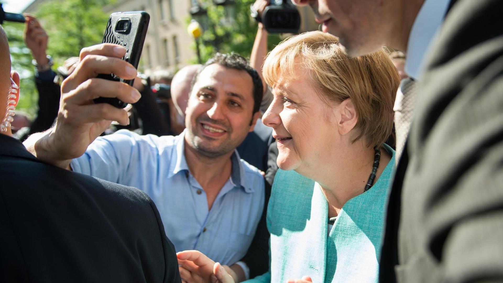 Bundeskanzlerin Merkel posiert in Berlin-Spandau mit einem Flüchtlinge für ein Selfie. Beide sind von Menschen umringt. Bundeskanzlerin Merkel posiert in Berlin-Spandau mit einem Flüchtlinge für ein Selfie. Beide sind von Menschen umringt.