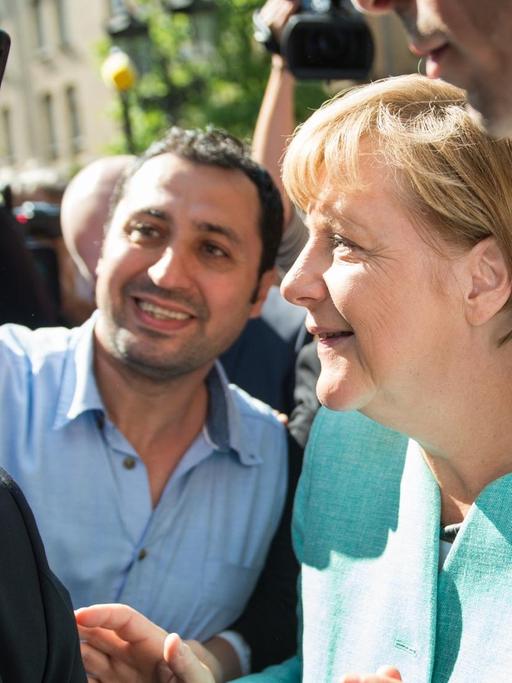 Bundeskanzlerin Merkel posiert in Berlin-Spandau mit einem Flüchtlinge für ein Selfie. Beide sind von Menschen umringt.