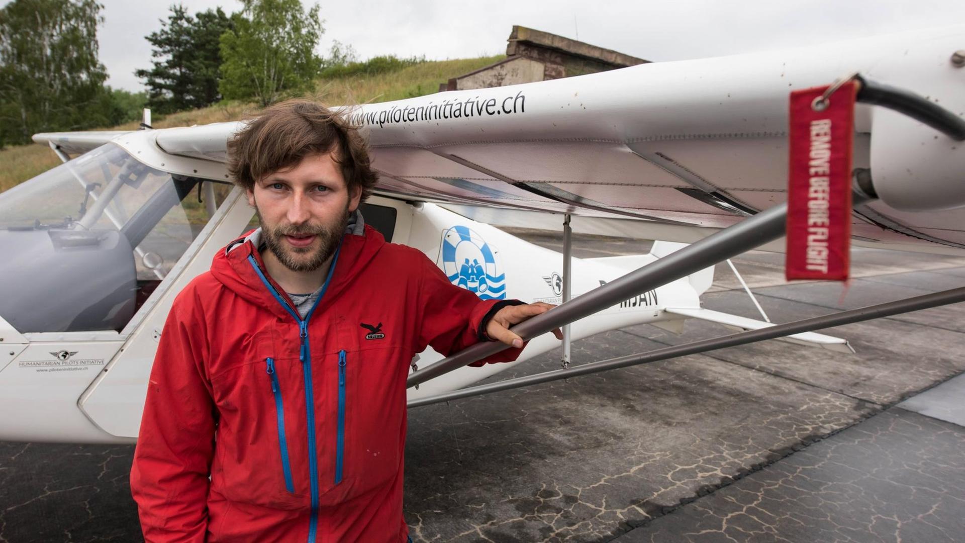 Farbfoto eines jungen bärtigen Mannes mit roter Jacke vor einem Ultraleichtflugzeug Farbfoto eines jungen bärtigen Mannes mit roter Jacke vor einem Ultraleichtflugzeug