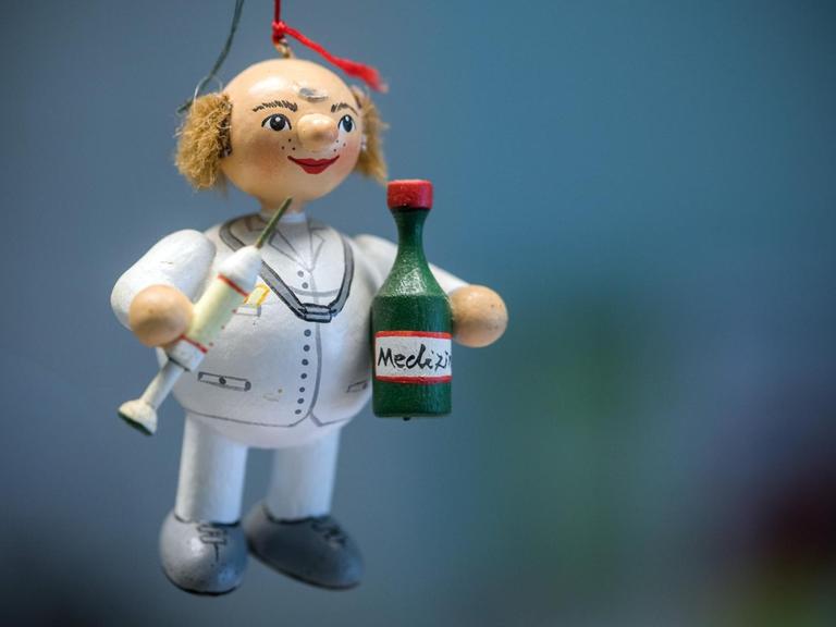 Eine Holzfigur eines Doktors mit Spritze und Medizinflächen hängt an einem roten Faden in einer Landarztparxis.