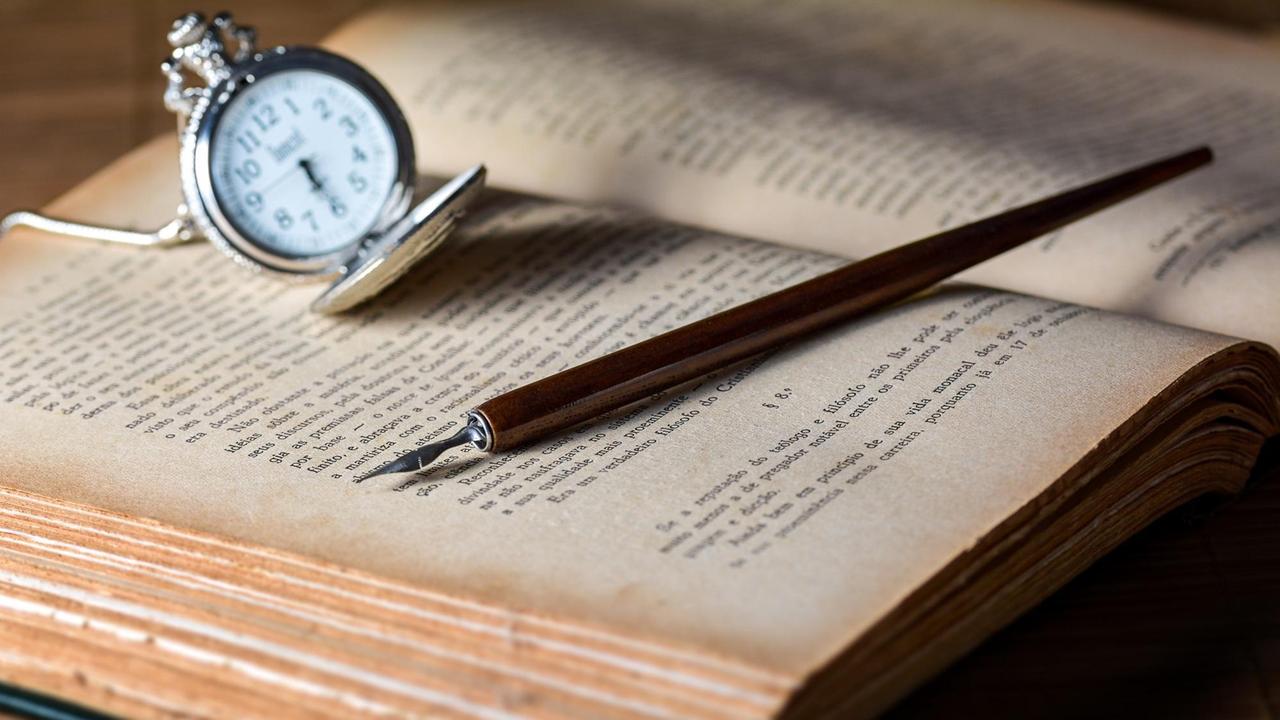 Eine alte Taschenuhr, daneben eine Tintenfeder auf einem aufgeschlagenen Buch. Eine alte Taschenuhr, daneben eine Tintenfeder auf einem aufgeschlagenen Buch.