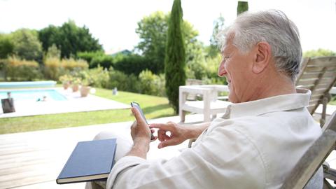 Ein Mann sitzt im Garten mit seinem Smartphone.