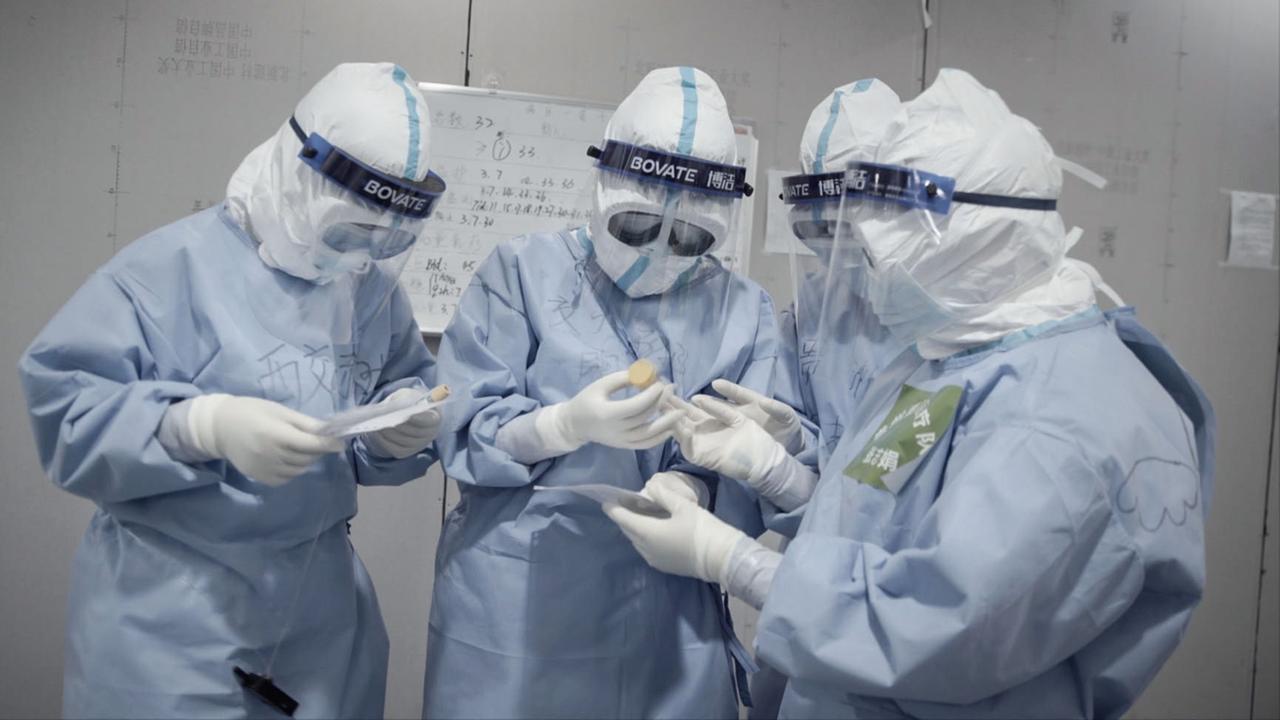 Vier Krankenschwestern im Schutzanzug betrachten Reagenzgläser mit Virenproben durch ihre Schutzbrillen. Vier Krankenschwestern im Schutzanzug betrachten Reagenzgläser mit Virenproben durch ihre Schutzbrillen.