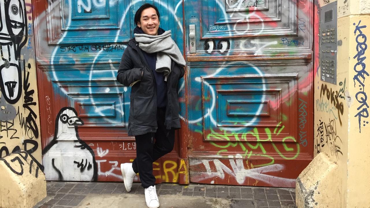 Der Berliner Modeschöpfer Hien Le steht an einem mit Graffiti besprühtem Hauseingang