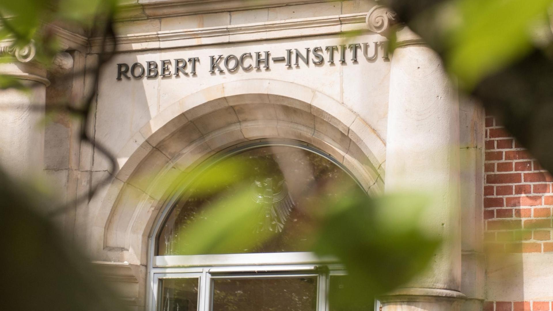 Der Eingang des Robert Koch-Instituts ist mit seinem Namenslogo durch Bäume hindurch zu sehen. Der Eingang des Robert Koch-Instituts ist mit seinem Namenslogo durch Bäume hindurch zu sehen.
