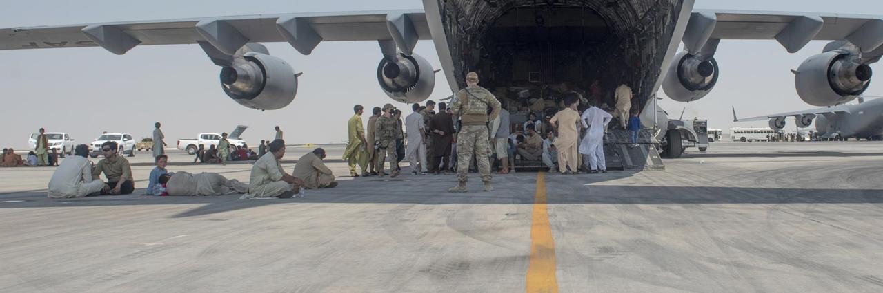 Menschen warten unter Begleitung der US Air Force unter den Flügeln eines Flugzeugs darauf, ausgeflogen zu werden. 
