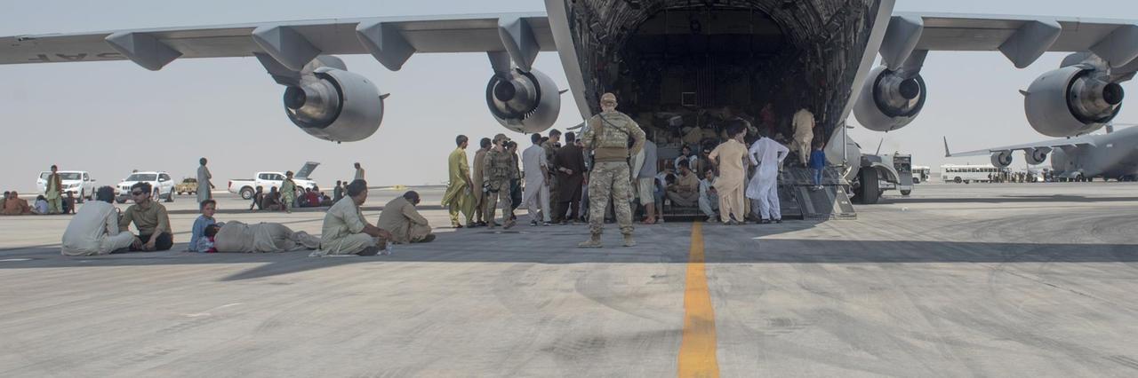Menschen warten unter Begleitung der US Air Force unter den Flügeln eines Flugzeugs darauf, ausgeflogen zu werden. Menschen warten unter Begleitung der US Air Force unter den Flügeln eines Flugzeugs darauf, ausgeflogen zu werden.