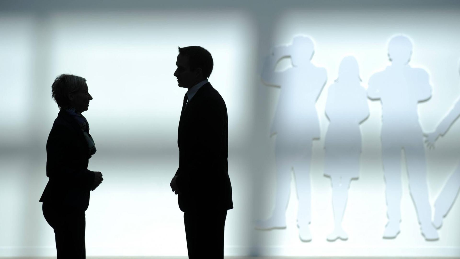 Die Silhouette eines Geschäftsmannes und einer Geschäftsfrau vor einer weißen Wand. Die Silhouette eines Geschäftsmannes und einer Geschäftsfrau vor einer weißen Wand.