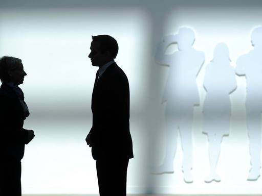 Die Silhouette eines Geschäftsmannes und einer Geschäftsfrau vor einer weißen Wand.