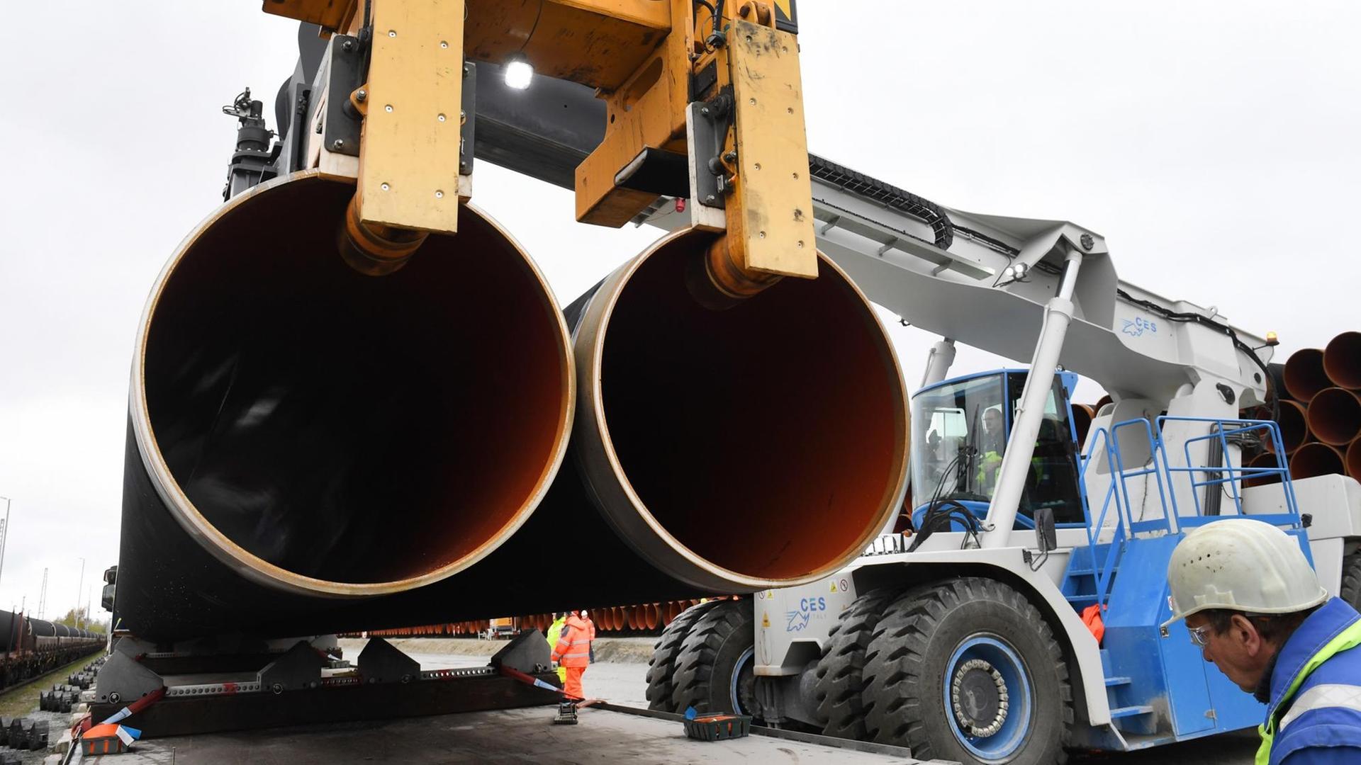 Ein Mann mit Schutzweste und Helm läuft im Fährhafen Sassnitz-Mukran auf Rügen zwischen zwei zu Türmen gestapelten Rohren für die geplante Gaspipeline Nord Stream 2 hindurch. Ein Mann mit Schutzweste und Helm läuft im Fährhafen Sassnitz-Mukran auf Rügen zwischen zwei zu Türmen gestapelten Rohren für die geplante Gaspipeline Nord Stream 2 hindurch.