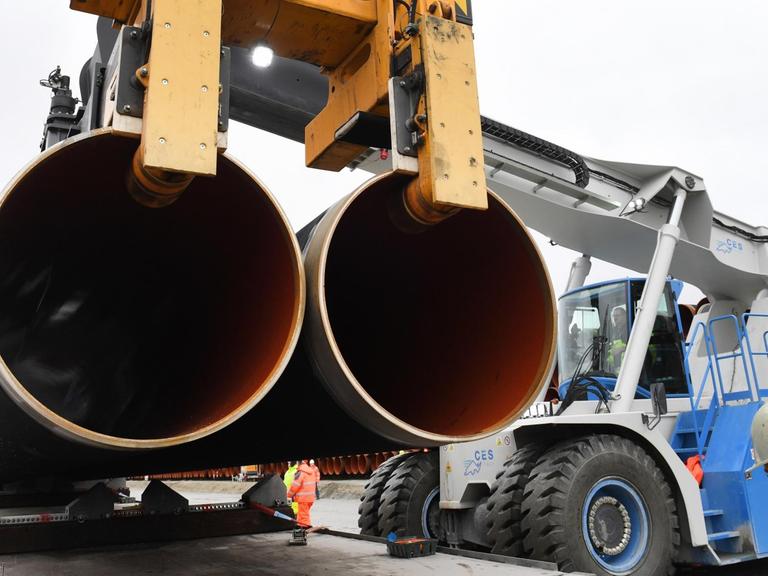 Ein Mann mit Schutzweste und Helm läuft im Fährhafen Sassnitz-Mukran auf Rügen zwischen zwei zu Türmen gestapelten Rohren für die geplante Gaspipeline Nord Stream 2 hindurch.