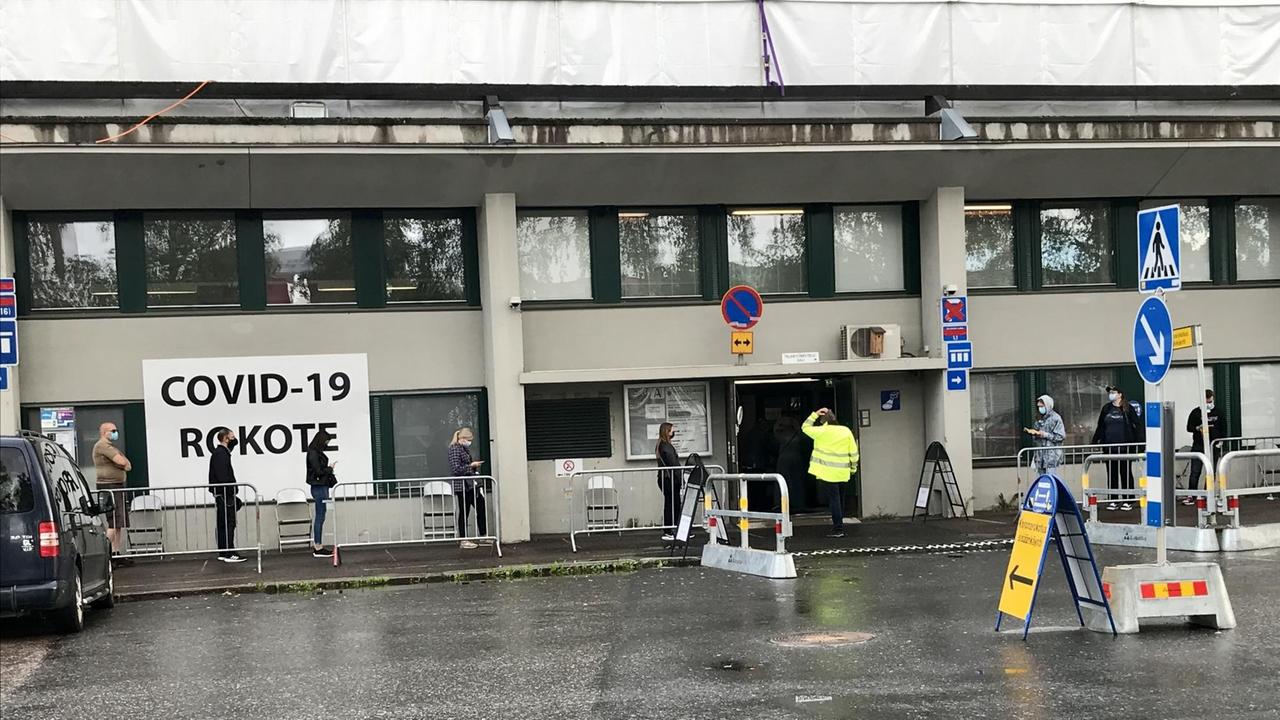 Menschen stehen vor einem Gebäude in der Schlange, an dem ein weißes Plakat mit der Aufschrift "Covid 19 - Rokote" angebracht ist. Menschen stehen vor einem Gebäude in der Schlange, an dem ein weißes Plakat mit der Aufschrift "Covid 19 - Rokote" angebracht ist.