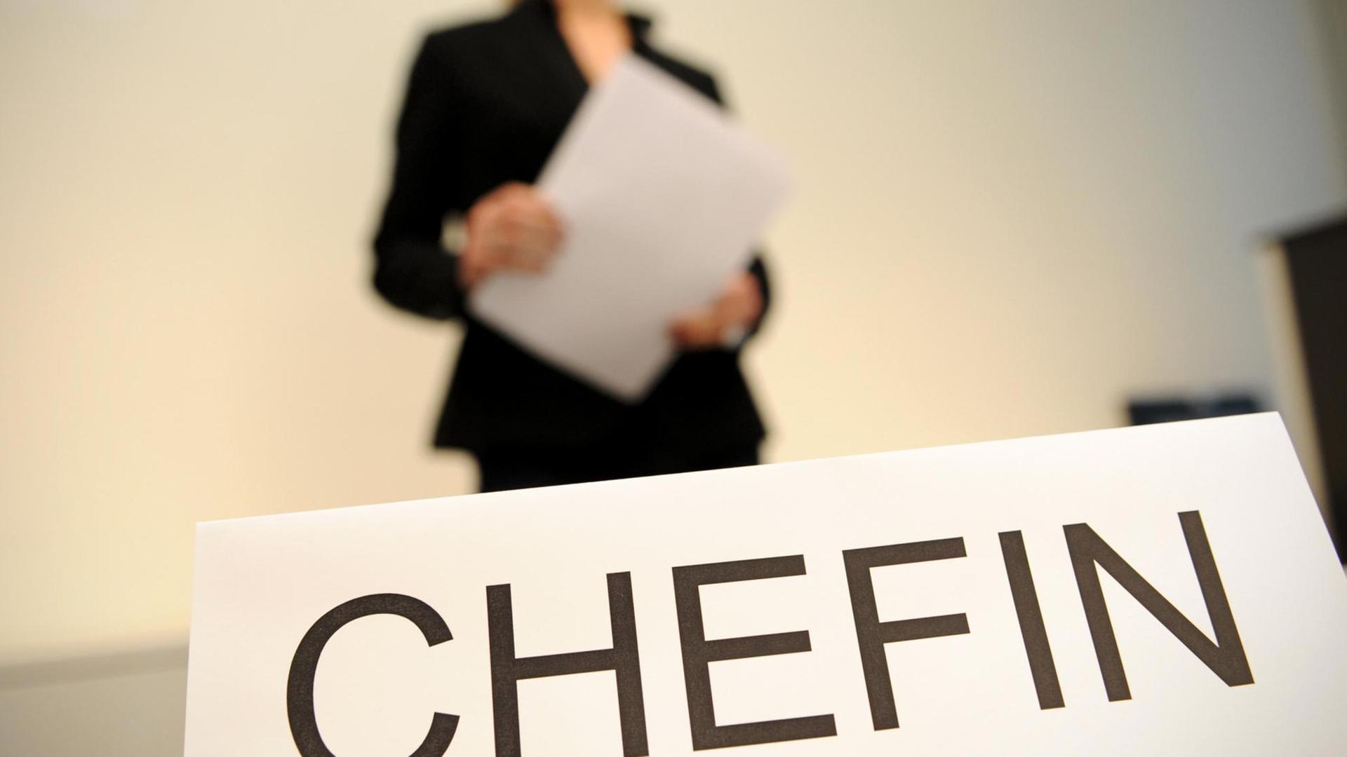 Eine Frau hält Papiere in der Hand. Vor ihr steht ein Schild mit der Aufschrift "Chefin". Eine Frau hält Papiere in der Hand. Vor ihr steht ein Schild mit der Aufschrift "Chefin".