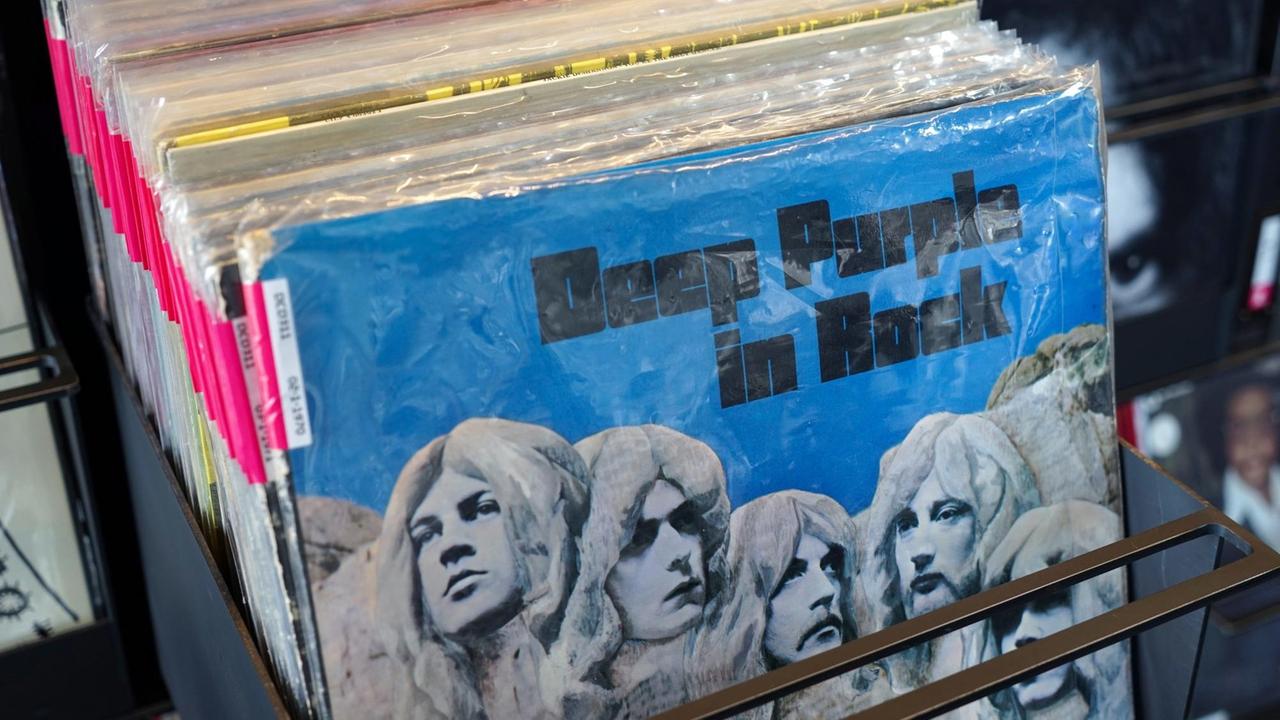 Ein Stapel Langspielplatten steht in einem Geschäft, das Cover der vordersten zeigt die Gesichter der Musiker als Steinreliefs: das Album "Deep Purple in rock"