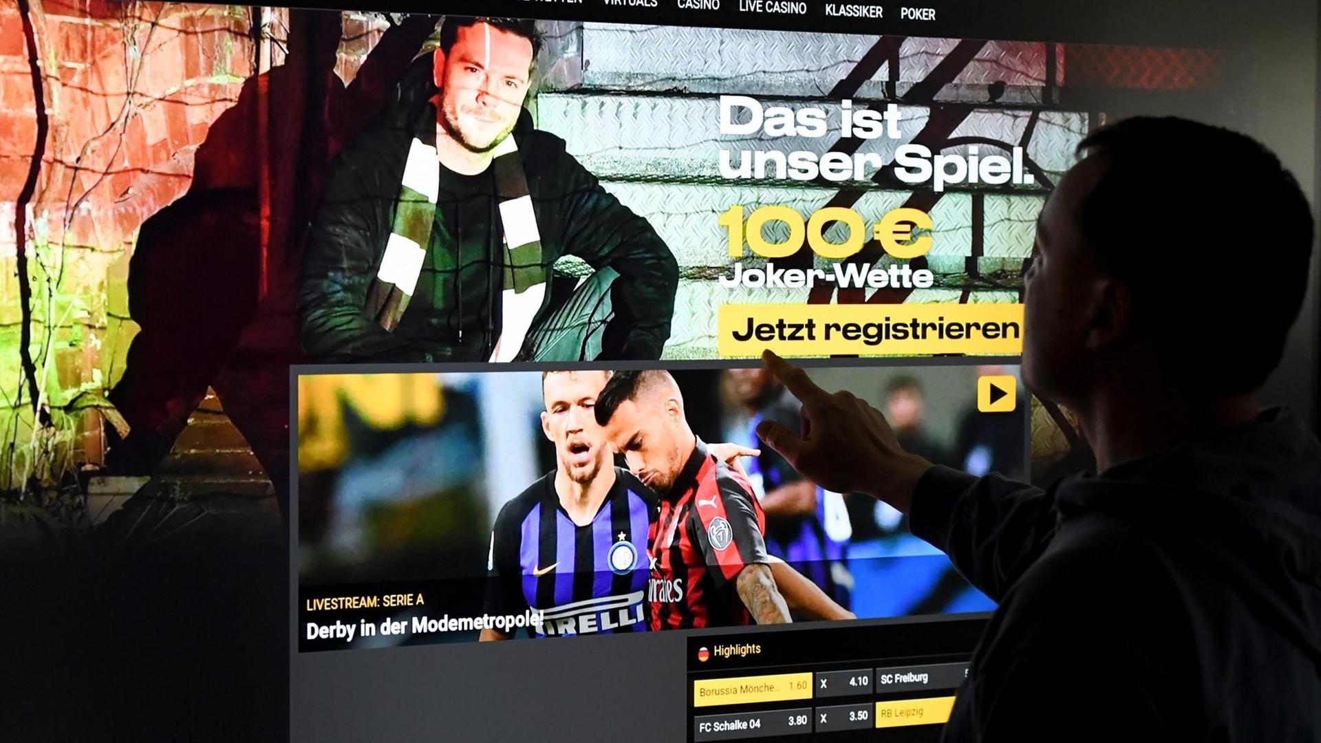 Ein Mann steht vor einem Bildschirm mit einer Seite eines Anbieters für Sportwetten Ein Mann steht vor einem Bildschirm mit einer Seite eines Anbieters für Sportwetten