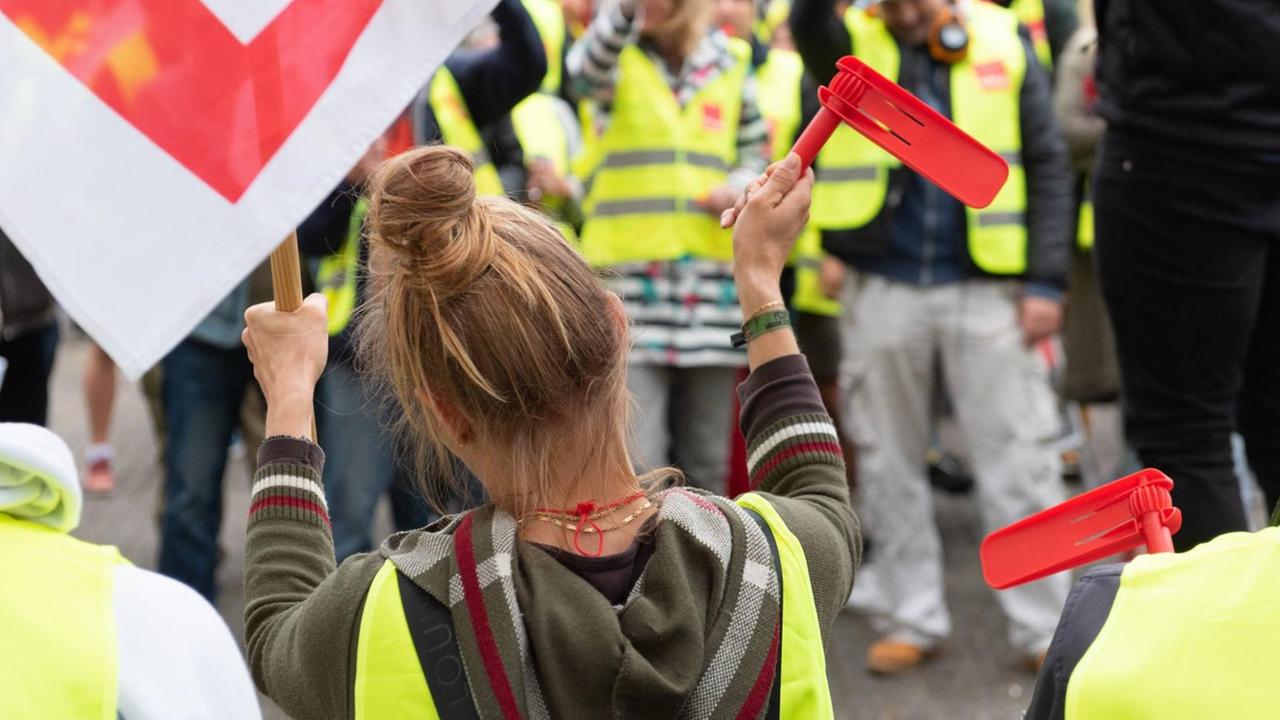 Eine Angestellte auf einem Streik, sie steht in einer Menschenmenge auf einer Kundgebung der Gewerkschaft "verdi" in Hamburg und schwenkt eine Fahne und hält eine rote Knatter Rätsche in die Luft. Eine Angestellte auf einem Streik, sie steht in einer Menschenmenge auf einer Kundgebung der Gewerkschaft "verdi" in Hamburg und schwenkt eine Fahne und hält eine rote Knatter Rätsche in die Luft.
