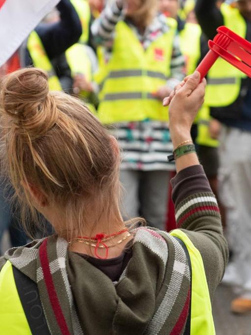 Eine Angestellte auf einem Streik, sie steht in einer Menschenmenge auf einer Kundgebung der Gewerkschaft "verdi" in Hamburg und schwenkt eine Fahne und hält eine rote Knatter Rätsche in die Luft.
