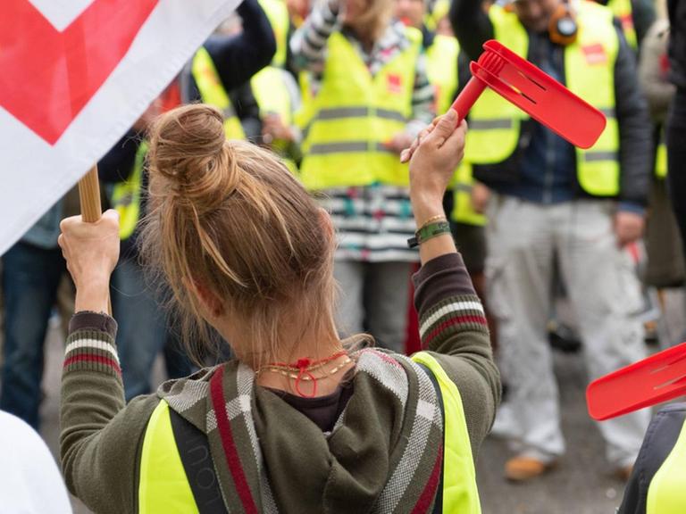 Eine Angestellte auf einem Streik, sie steht in einer Menschenmenge auf einer Kundgebung der Gewerkschaft "verdi" in Hamburg und schwenkt eine Fahne und hält eine rote Knatter Rätsche in die Luft.