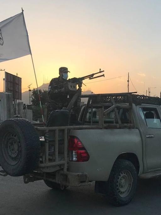 Taliban, bewaffnet, stehen auf einem Pick-up.