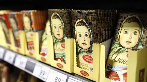 In einem Supermarktregal sind Schokoladentafeln aufgereiht. Darauf zu sehen ist ein Mädchen mit bäuerlichem Kopftuch.