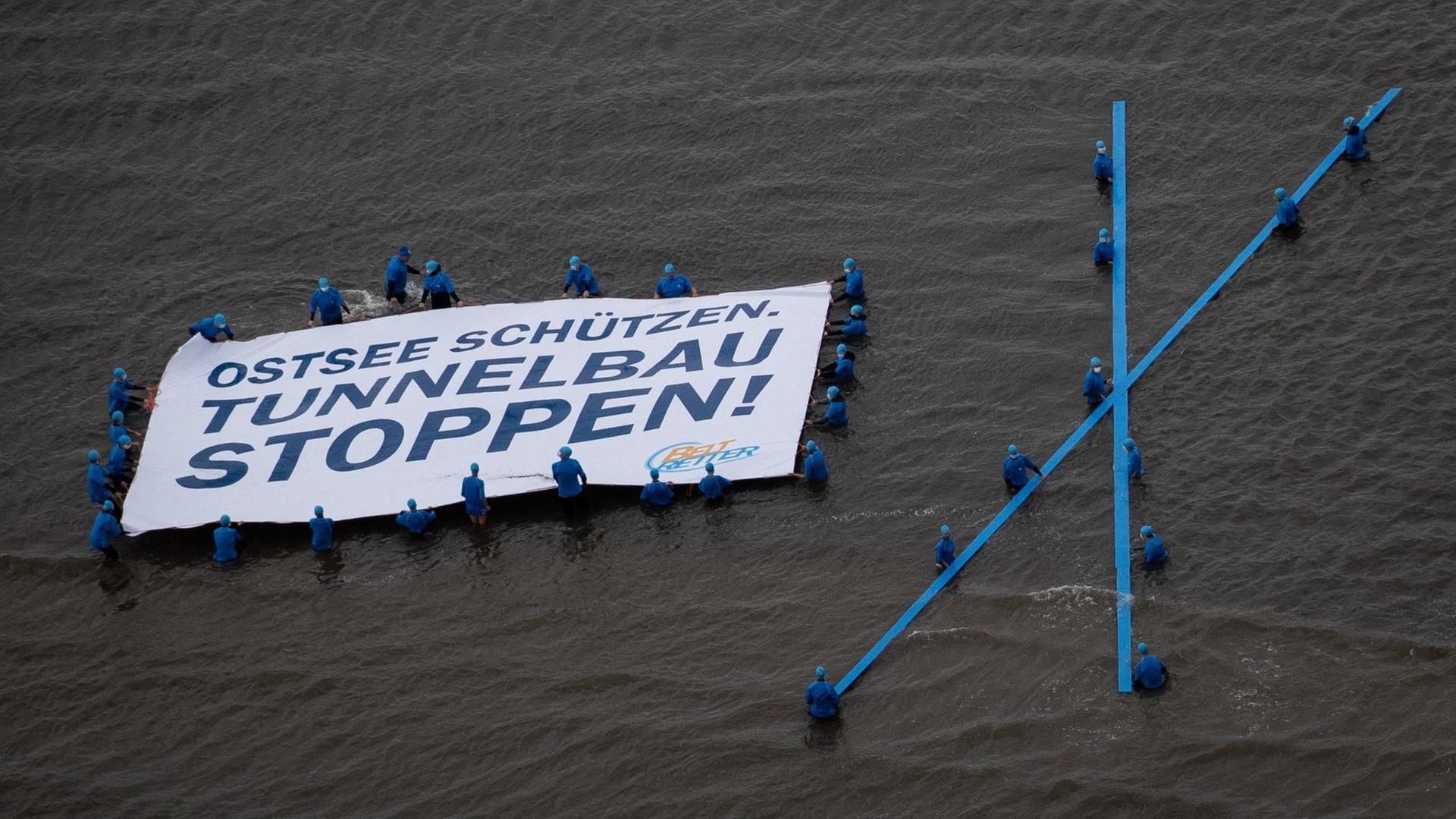 Demonstrierende mit einem Banner im Wasser, auf dem "Ostsee schützen. Tunnelbau stoppen!" steht Demonstrierende mit einem Banner im Wasser, auf dem "Ostsee schützen. Tunnelbau stoppen!" steht