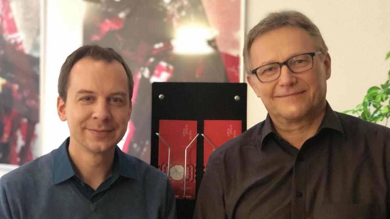 Die beiden Leiter stehen vor einem Aufsteller mit Konzertflyern des aktuellen Jahrgangs. Die beiden Leiter stehen vor einem Aufsteller mit Konzertflyern des aktuellen Jahrgangs.