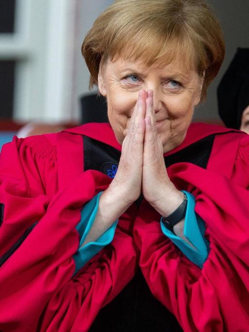 Kanzlerin Angela Merkel trägt eine rote Robe der Harvard-Universität und hat die Hände vor ihrem lächelnden Gesicht zu einer Dankesgeste zusammengelegt, nachdem sie die Ehrendoktorwürde verliehen bekam