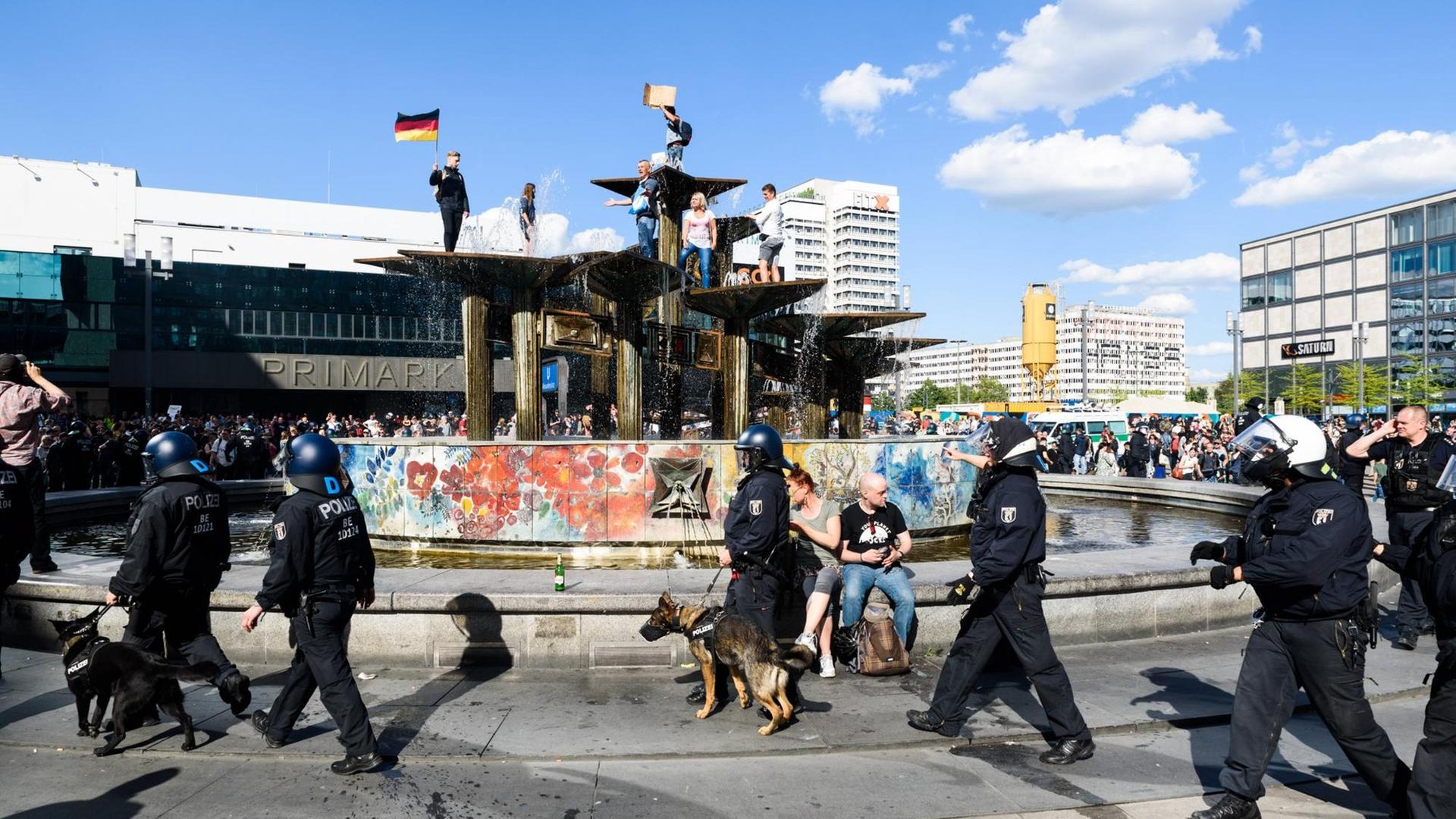 Vor dem Brunnen auf dem Alexanderplatz in Berlin gehen Polizisten. Dahinter haben Demonstranten den Brunnen bestiegen. Vor dem Brunnen auf dem Alexanderplatz in Berlin gehen Polizisten. Dahinter haben Demonstranten den Brunnen bestiegen.