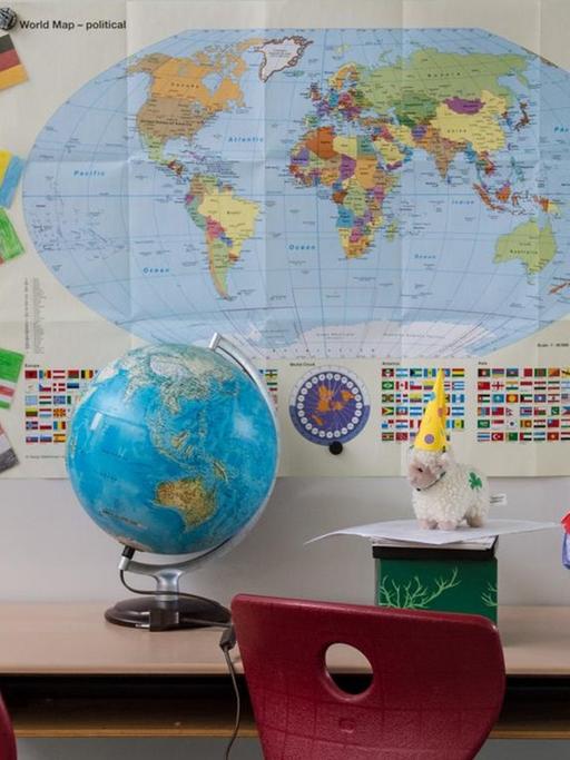 Eine Schulbank mit einem Globus, im Hintergrund eine Weltkarte