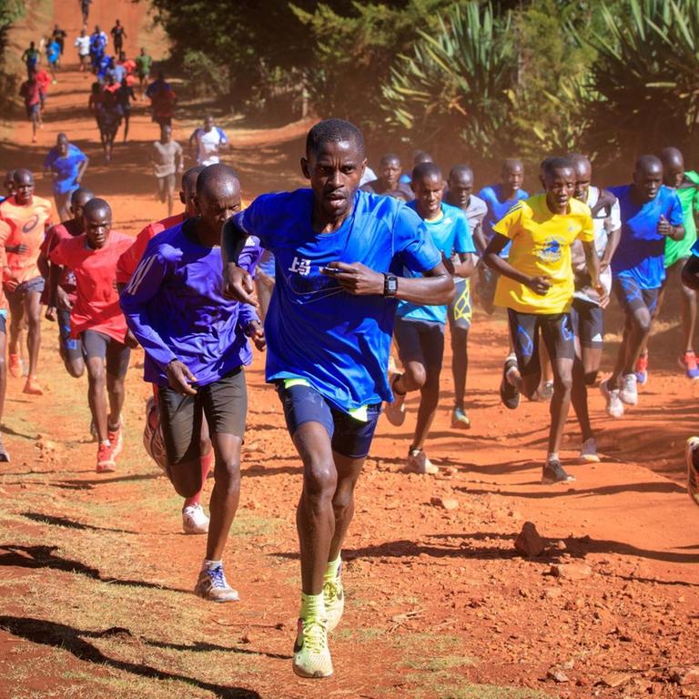 Junge Läufer sind auf einer Straße im roten Sand rund um die Kleinstadt Iten im hügeligen Hochland Kenias unterwegs