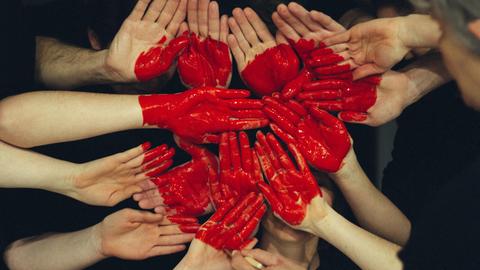 Ein Herz aus roter Farbe und vielen Händen.