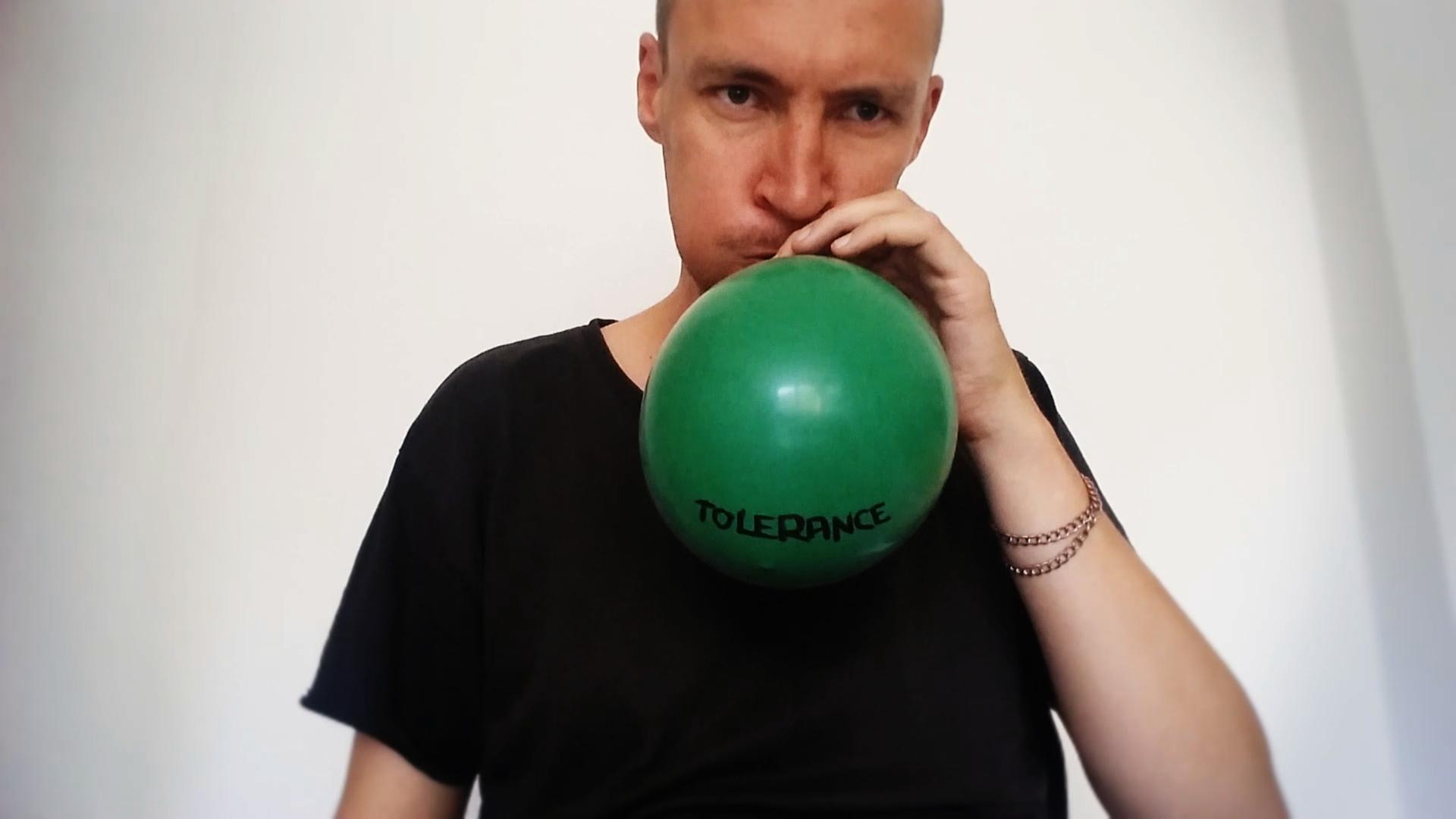 Der Audio- und Videokünstler Kuesti Fraun bläst einen grünen Luftballon auf mit der Beschriftung "Tolerance"