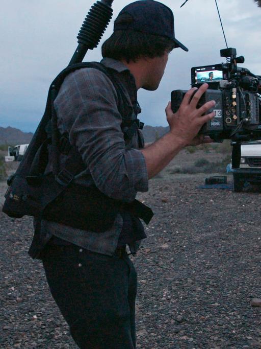 Regisseurin Chloé Zhao, Kameramann Joshua James Richards und Frances McDormand beim Dreh zu "Nomadland". Vor karger Landschaft und bewölktem Himmel.